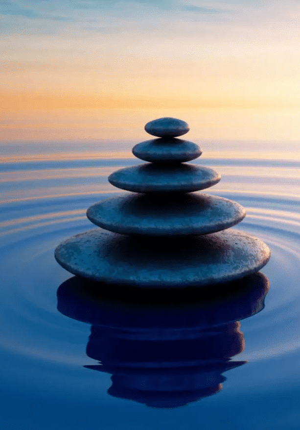 Stack of balanced stones on calm water at sunset.
